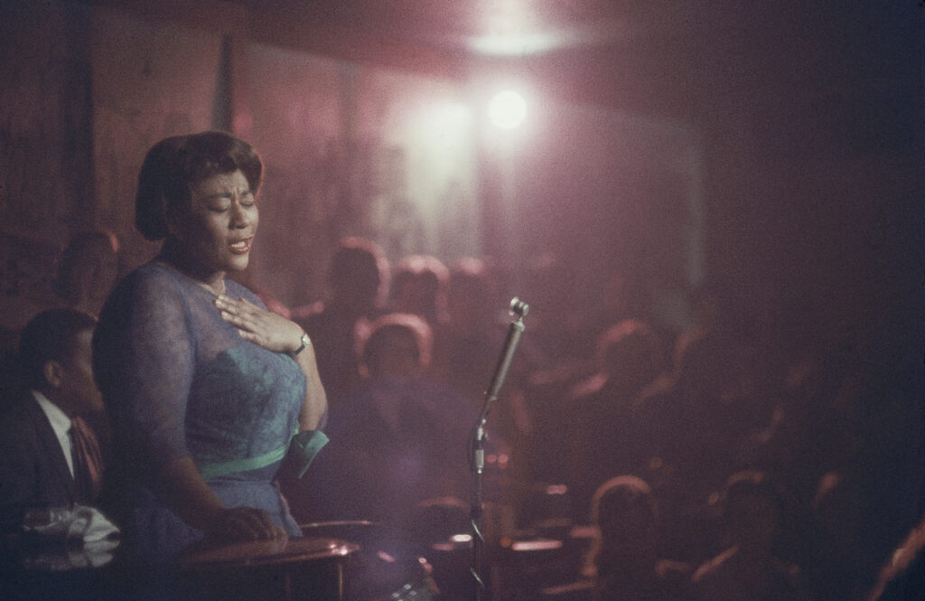 Bathed in red light, American jazz singer Ella Fitzgerald performed her eyes closed, at Mister Kelly's nightclub, Chicago, 1958.