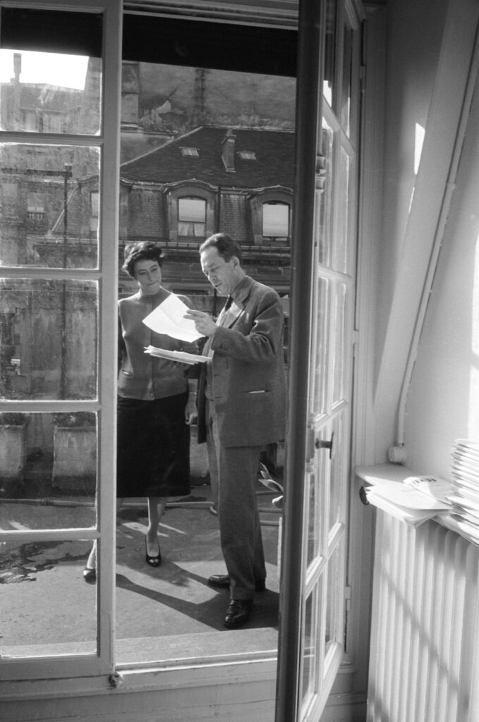 French author and philosopher Albert Camus stands with an unidentified woman and reads one of a number of letters on a balcony outside his publishing office, Paris, 1957.